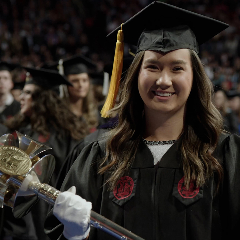 A student carrying the university mace leads the commencement entrance.