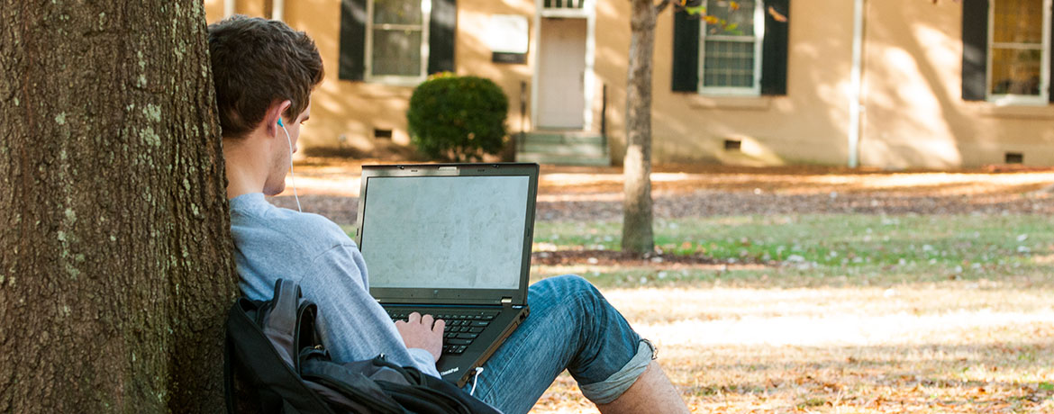 student typing on a laptop outdoors on the Horseshoe
