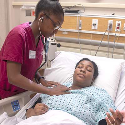 Nursing student listening to a patient's heart with a stethoscope.