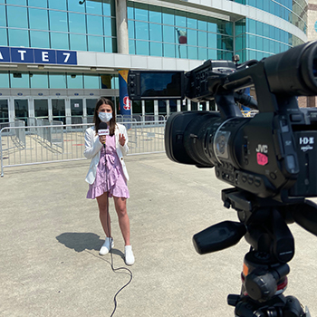 A sports journalism student broadcasts in front of a stadium.