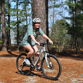 Student riding a bike in a wooded park.