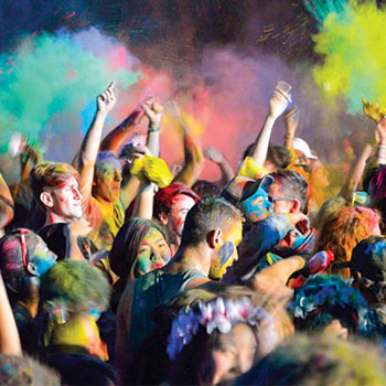 Large gathering of people at a color run  covered in colored chalk dust and clouds of it in the air.