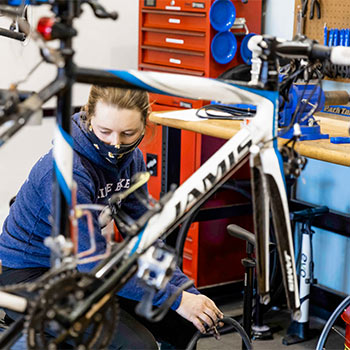 Student working in the bike shop with a bike in front of her.
