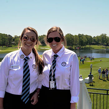 Students in a uniform standing on a balcony overlooking a golf course. 