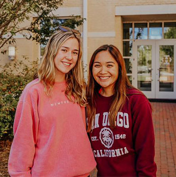 Two students standing infront of a residence hall smiling at the camera. 