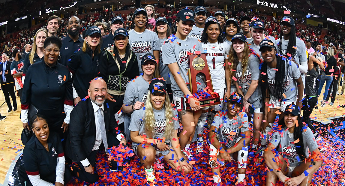 The Gamecock Women's Basketball team and support staff smiling at the camera at center court with their NCAA trophy and confetti raining down on them.