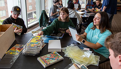 Group of students sitting at a large table with comic books stacked up.