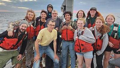 A research group gathered together on a boat wearing life jackets and smiling at the camera.
