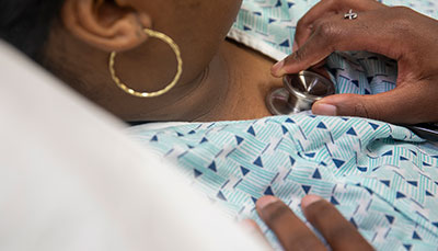 Person holding a stethoscope to a patient's chest.