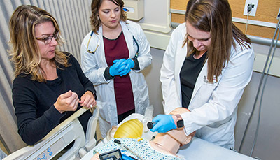 Professor and two students practicing on a nursing mannequin in a simulation lab