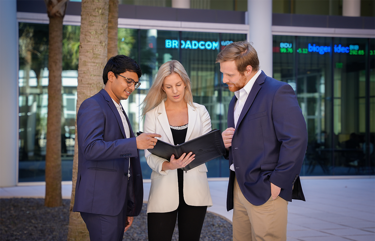 Three business professionals looking at a notebook together in an outdoor courtyard. 