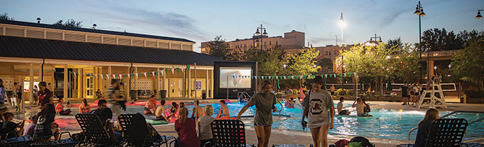 The outdoor pool at the fitness center at dusk with people hanging out getting ready to watch a movie at the Dive-In Movie event. 