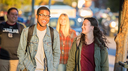 Two students laughing with each other as they walk down the city street. 