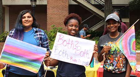 Three students smiling holding LGBTQ+ flags they made. 