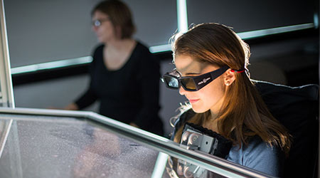 Student looking through a piece of glass with 3D glasses on. 