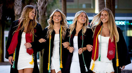 Four graduates linking arms and walking. 