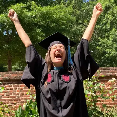 Graduate with her arms raised in celebration.