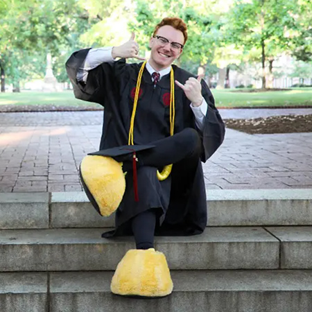 Graduate sitting on the steps on the Horseshoe wearing Cocky feet. 