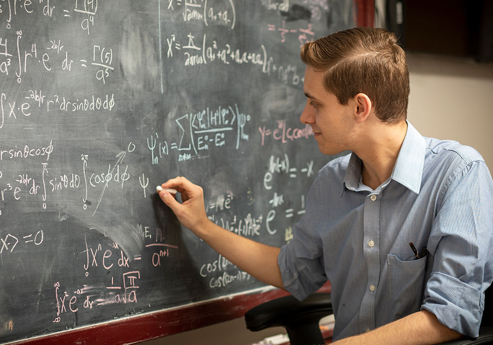 Eric writes mathematical formulas on a chalkboard.