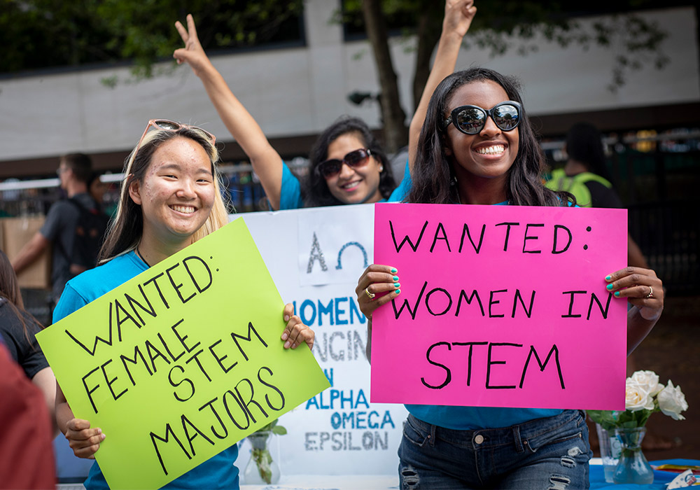 Students holding signs at the student organization fair that say Wanted: female STEM majors.