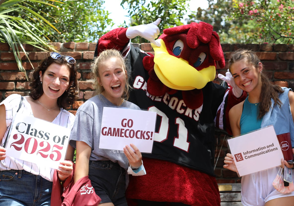 Three UofSC College of Information and Communications students pose with Cocky for a photo.