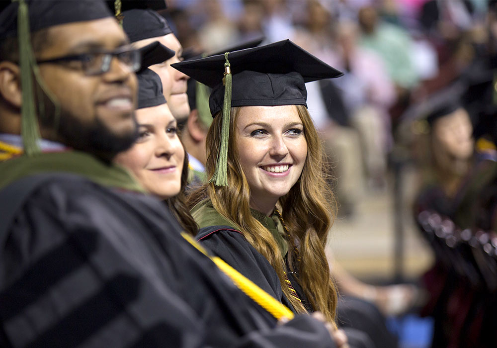 Student smiling at a commencement ceremony wearing a graduation cap and gown.