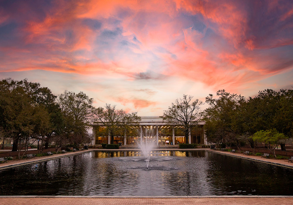 Thomas Cooper library sits behind the fountains of the reflecting pond in front of a stunning purple and red sunset. 
