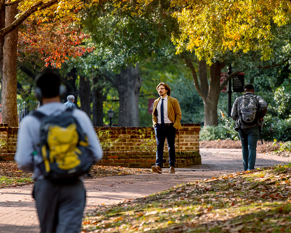 Faculty member walking down a path surrounded by fall trees.