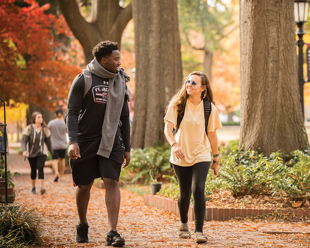 Two students walking down the brick path on a beautiful fall day.