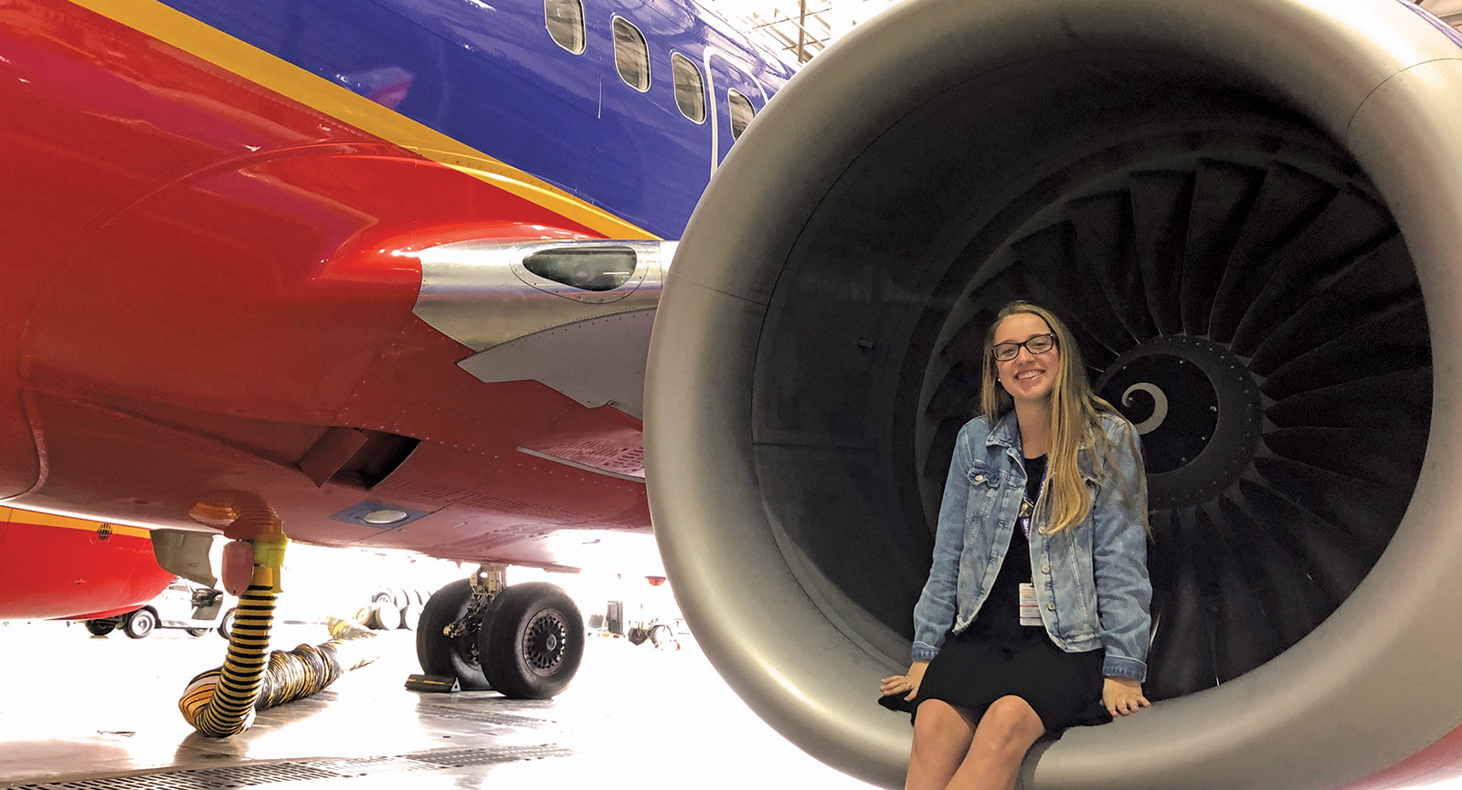 Megan Gallagher sits on the booster engine of a Southwest Airlines plane parked in hanger. 