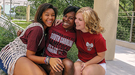 Three students wearing UofSC t-shirts laughing together.