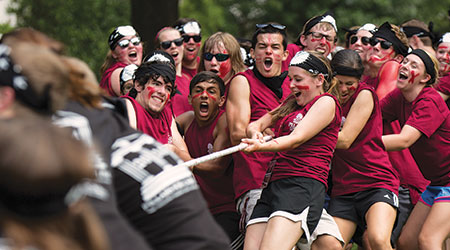 Students wearing garnet and black shirts playing an intense game of tug-of-war wearing facepaint. 