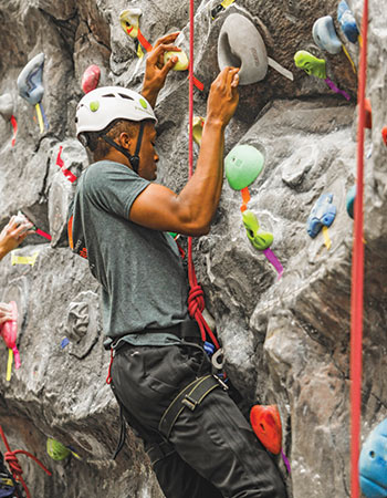 Student waring a helmet and a harness climbing the indoor rock wall.