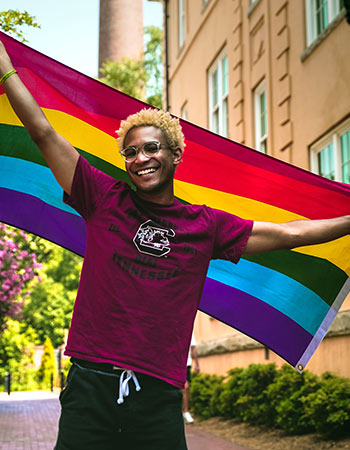 Student wearing a Gamecock t-shirt holding a pride flag. 