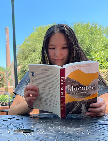 Student at an outdoor table reading the First Year Reading Experience book. 
