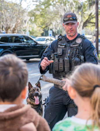 A police officer with a K-9 officer speaks to children.