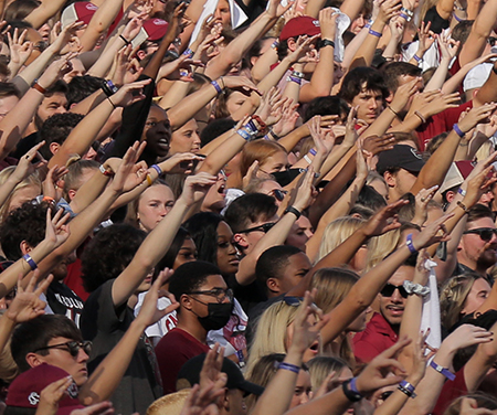 Crowd of fans at a football game with their arms raised.