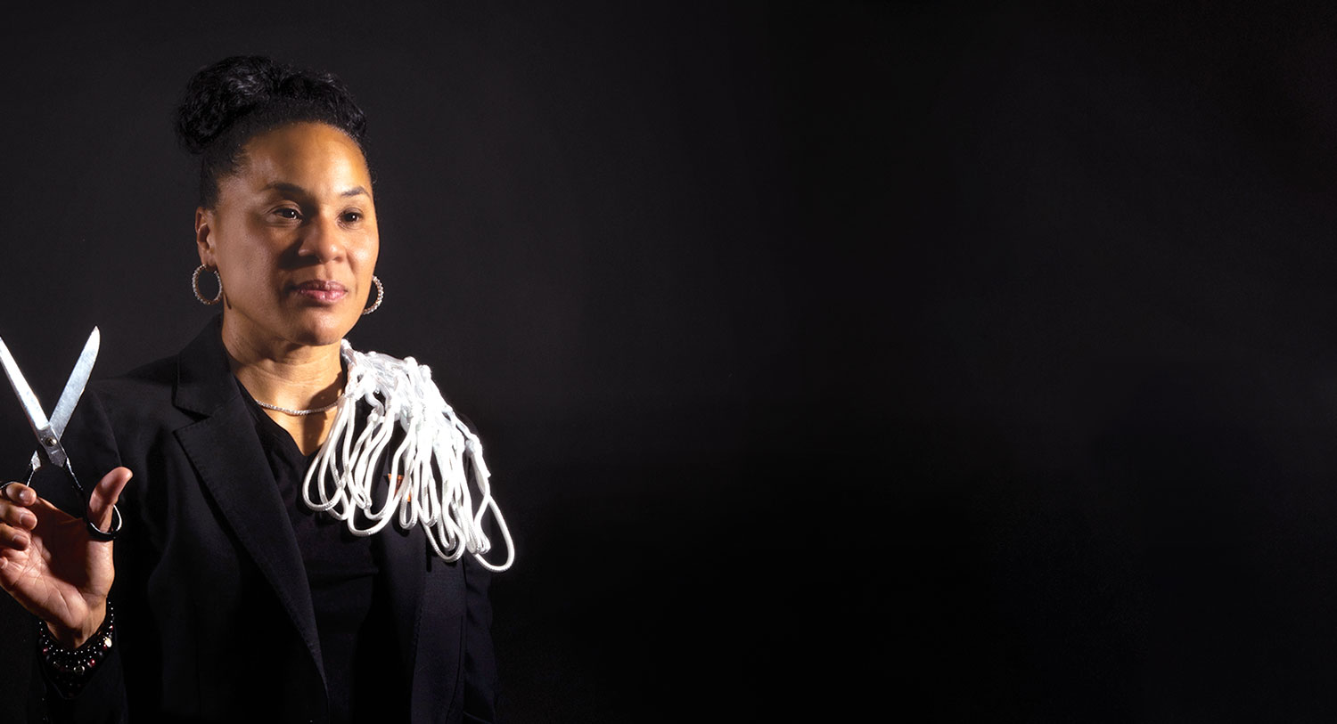 A studio portrait of Dawn Staley with net and scissors in hand.