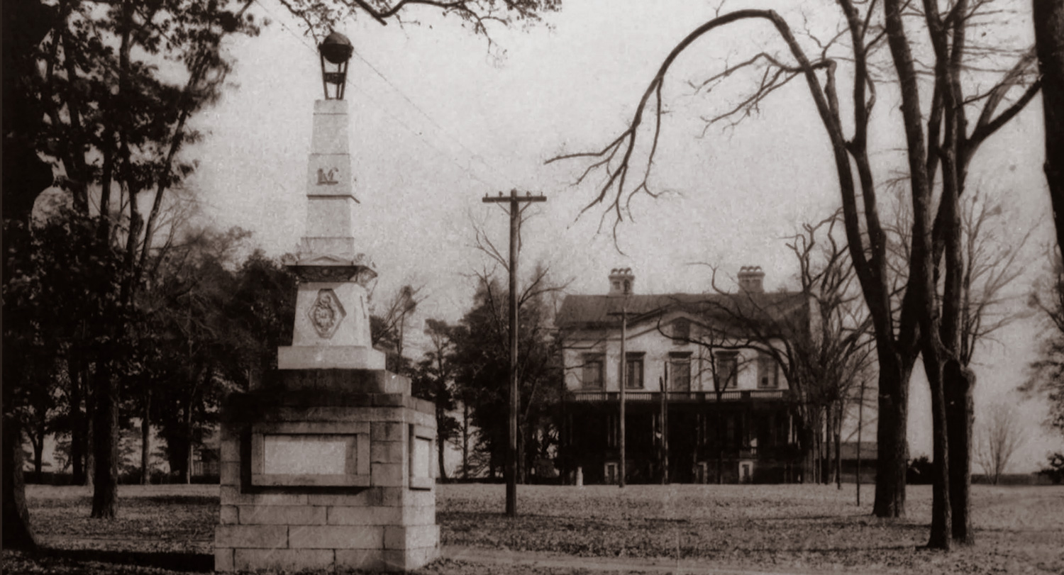 This 1905 historic photograph features the Maxcy Monument standing in the center of the Horseshoe at the University of South Carolina in Columbia, South Carolina. In the background, you can see the university's original, historic President's House.