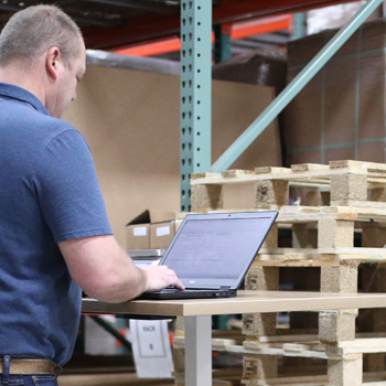 a man enters information on a laptop inside a warehouse