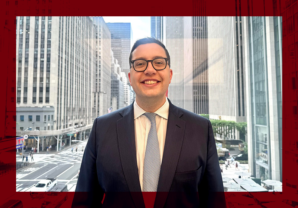 University of South Carolina alumnus Adam Lemp stands in a New York City office overlooking a downtown street, with Radio City Music Hall visible in the background.