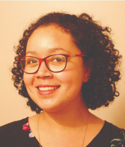 Claire Jimenez wears black and red glasses and a black and red shirt, has curly hair, and smiles at the camera in a close-up.