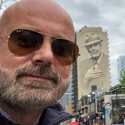 Dr. Mark Smith stands in front of a Leonard Cohen mural