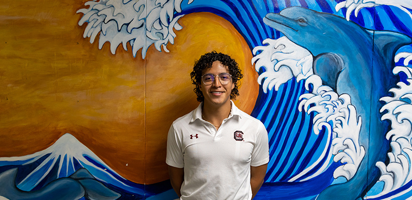 Diego stands in front of an ocean mural. 