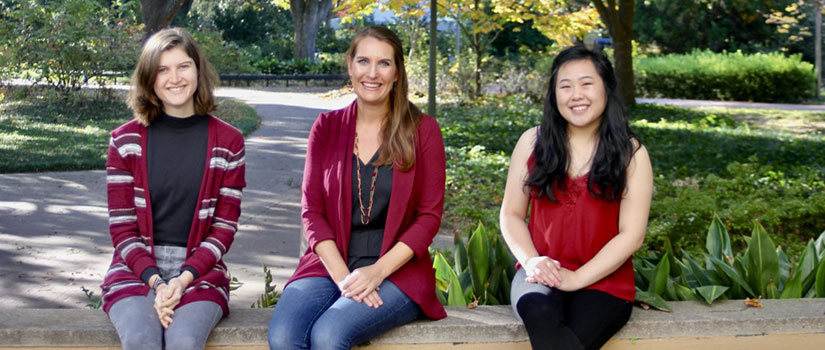 Three women sit on brick steps with garnet sweaters and smile. 