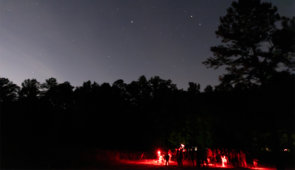 Visitors gather at night using red lights to protect night vision during a stargazing event.
