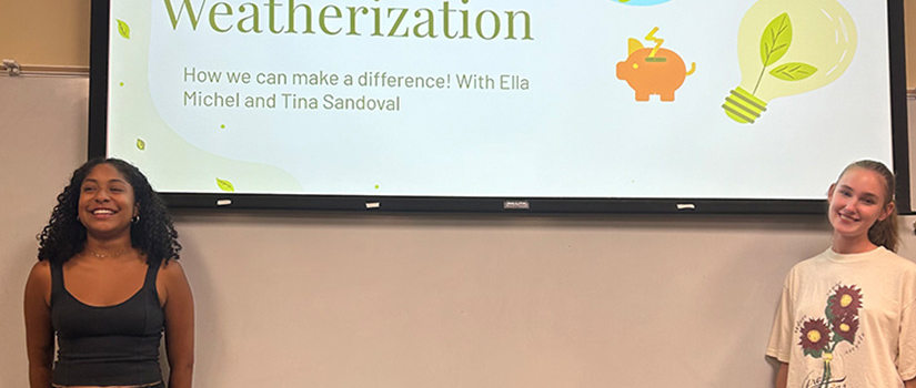 Ella Michel and Tina-Maria Sandoval standing in front of a presentation slide titled 'Energy Efficiency and Weatherization: How we can make a difference!' The slide includes icons of a globe, a light bulb, and a piggy bank with a lightning bolt.