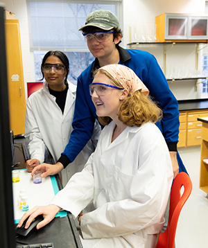 three students in lab coats looking at a computer screen