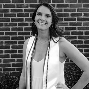 Black and white image of Kylie hurst in white graduation dress and cords.