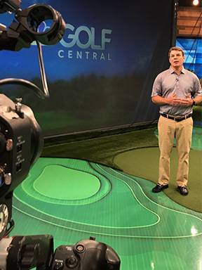 Justin Tupper stands with cameras filming a segment on a faux putting green.